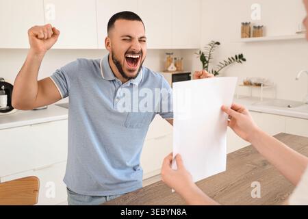 Felice giovane uomo e sua moglie con modulo di rimborso in cucina Foto Stock