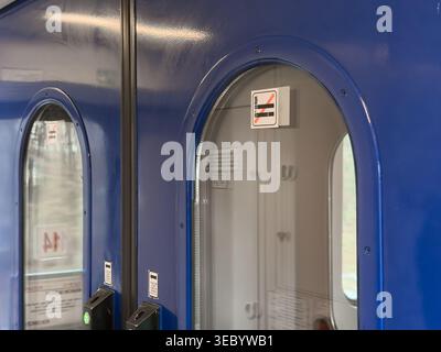 Primo piano di una vivace porta blu del treno con due finestre rotonde, una con il simbolo di divieto di fumo, che indica un ambiente non fumatori per i viaggi Foto Stock