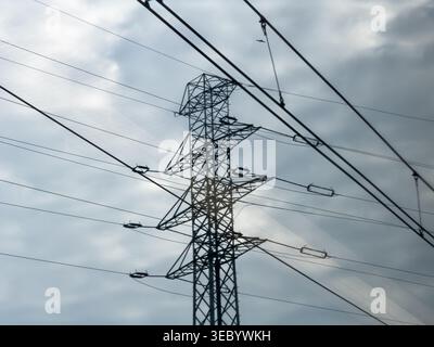 Una torre sagomata in pilone elettrico ad alta tensione con un'intricata struttura a reticolo in acciaio si erge in modo prominente contro un cielo nuvoloso e spettacolare Foto Stock