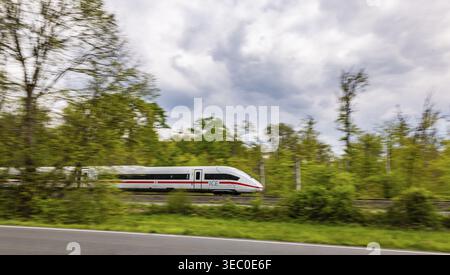 Binari ferroviari vicino a Moerfelden-Walldorf. Un GHIACCIO viaggia su un percorso aperto attraverso una foresta. Trascinamento, sfocatura del movimento. Moerfelden-Walldorf, Baden-Wuerttemberg Foto Stock