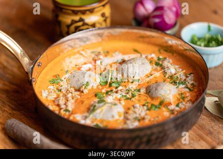 Questo colpo impressionante cattura un saporito curry kofta di polpette indiano servito in una padella rustica. La cremosa salsa d'arancia e le decorazioni fresche sono inviti Foto Stock
