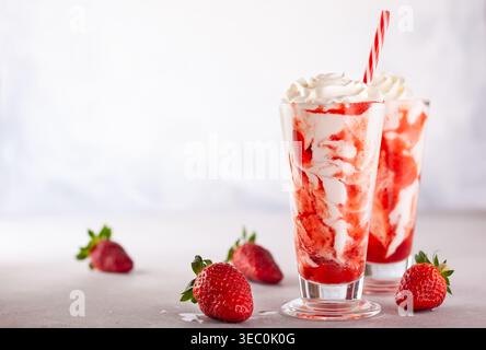 Frullato di fragole con panna montata e sciroppo di bacche nel bicchiere alto su sfondo chiaro. Foto Stock