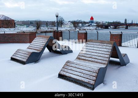 Bellissime panchine doppie coperte di neve sulla riva del fiume. Panchine sul balcone del molo, recintate con barriera metallica. Molo cittadino. Foto Stock