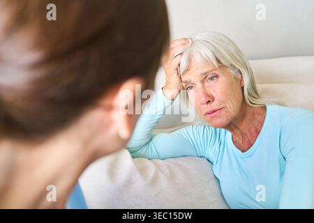 Una donna anziana esprime le sue preoccupazioni per la salute, apparendo angosciata mentre parla con un medico o un caregiver. Foto Stock