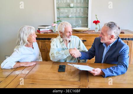 Una coppia senior si occupa di pianificazione pensionistica e discussioni sulla sicurezza finanziaria, stringendo la mano a un consulente professionale. Foto Stock