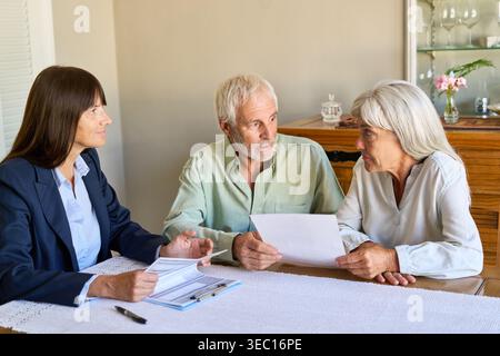 Una coppia di anziani è impegnata in una discussione seria sulla pianificazione pensionistica e la protezione finanziaria con un consulente professionale a casa. Foto Stock
