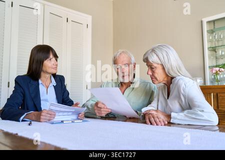 Una coppia di anziani si occupa di pianificazione pensionistica e di discussioni sulla protezione finanziaria con un consulente professionale, esaminando documenti importanti presso un'a ta Foto Stock