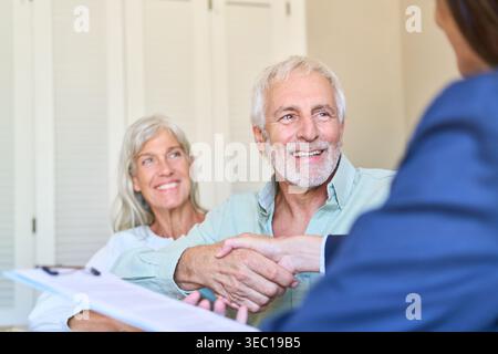 Una coppia senior si occupa di pianificazione pensionistica e protezione finanziaria, stringendo la mano a un consulente finanziario. Foto Stock