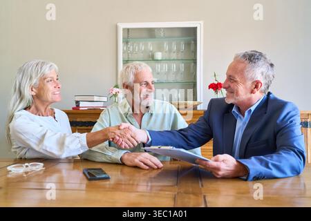 Una coppia senior si occupa di pianificazione pensionistica e protezione finanziaria, stringendo la mano a un consulente finanziario. Foto Stock