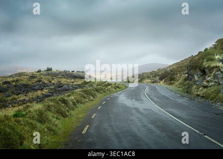 La strada N71 del Ring of Kerry passa attraverso terreni di montagna selvaggi e formazioni rocciose glaciali nella campagna irlandese. Foto Stock