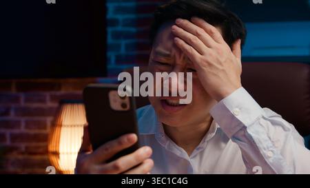 Turbato ha sottolineato il fallimento di un uomo d'affari asiatico di mezza età con il telefono cellulare di sera ufficio triste frustrato uomo d'affari coreano con smartphone guasto Foto Stock
