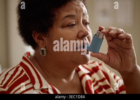 Donna anziana di colore che usa l'inalatore per il trattamento dell'asma a casa Foto Stock