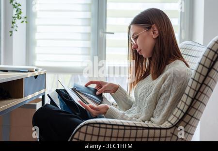 Donna che gestisce il lavoro creativo con tavolozze di colori e laptop in una comoda poltrona Foto Stock