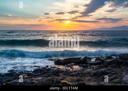 Tramonto sul mare con onde e costa rocciosa Foto Stock