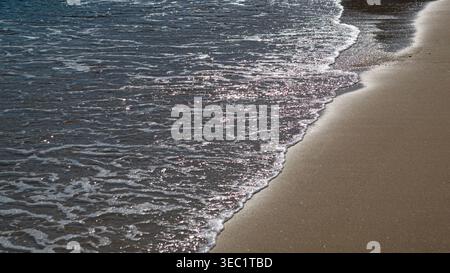 Le onde del mare si lavano su una spiaggia sabbiosa dorata Foto Stock