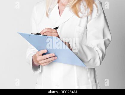 Professionale in camice bianco prendere appunti sugli appunti in ambiente clinico Foto Stock