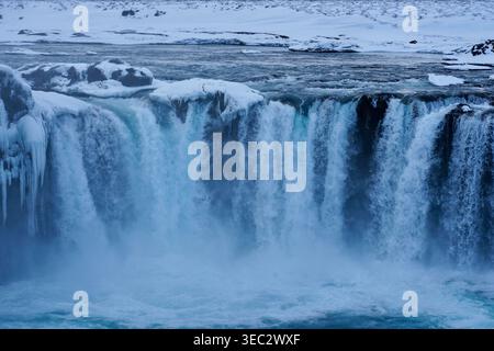 Cascata ghiacciata in paesaggio invernale con scogliere coperte di neve e cascata azzurra nebbiosa Foto Stock