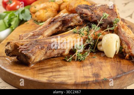 Primo piano di costolette di agnello grigliate con timo fresco e aglio arrosto servite su un piatto rustico di legno. Foto Stock