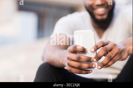Uomo che utilizza lo smartphone all'aperto, gode del tempo libero con un sorriso e una postura rilassata Foto Stock