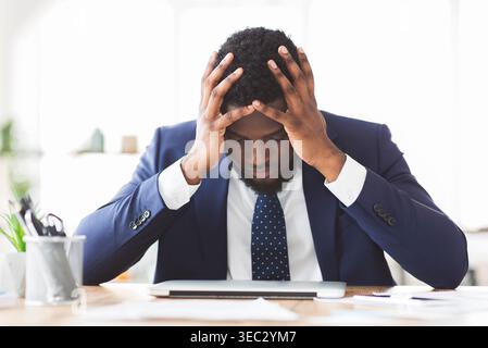 Sottolineato imprenditore seduto in ufficio con la mano sulla fronte Foto Stock