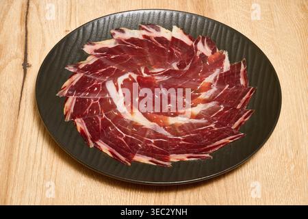 Deliziose fette di tradizionale prosciutto iberico spagnolo preparato su un piatto scuro, pronto per la degustazione Foto Stock