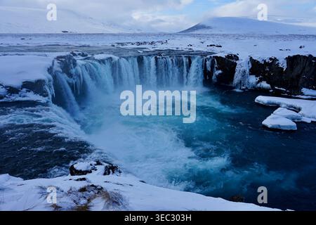 Cascata invernale nel paesaggio artico innevato con scogliere ghiacciate e piscina turchese Foto Stock