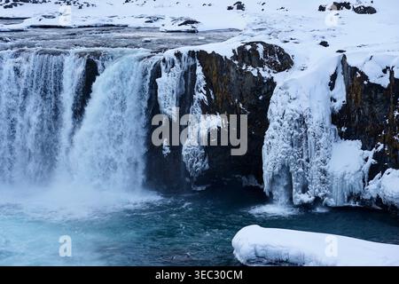Cascata ghiacciata e scogliere ghiacciate nel paesaggio invernale innevato con il fiume Turchese Foto Stock