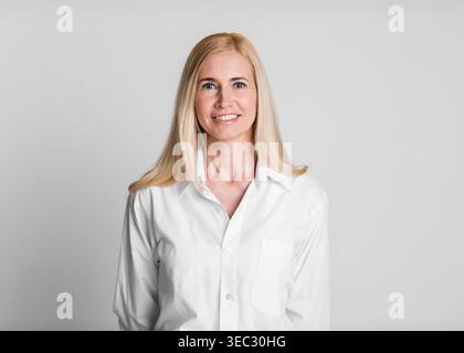Donna sorridente in una camicia bianca che posa su uno sfondo grigio chiaro in un ambiente Studio Foto Stock