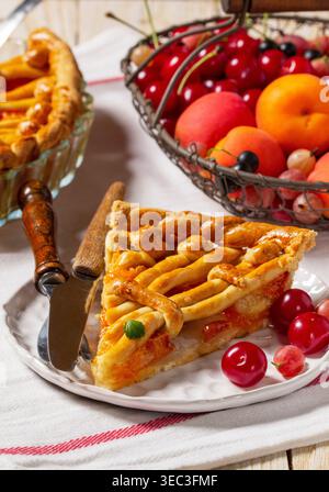 Torta di albicocche decorata con decorazioni a base di impasto e un cestino di metallo con frutta e frutti di bosco. Foto Stock