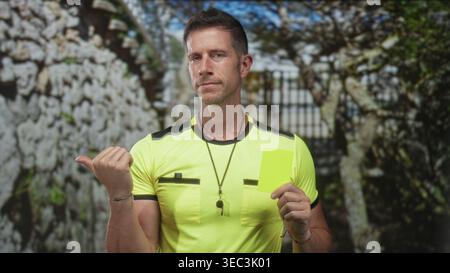 L'uomo punta il pollice e tiene il cartellino giallo accanto al cancello di pietra all'ingresso dell'edificio; sport dell'autorità di applicazione delle regole. Foto Stock