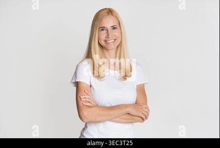 Giovane donna sorridente con fiducia mentre si trova in piedi contro un background semplice in abbigliamento casual Foto Stock
