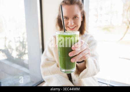 Ritratto di una giovane donna sorridente seduta in un bar con un bicchiere di latte matcha ghiacciato Foto Stock