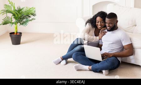 Giovane coppia che lavora insieme su un notebook mentre si siede comodamente sul pavimento Foto Stock