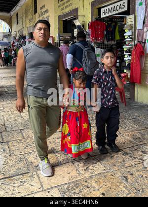 Uomo del posto che cammina con i suoi due figli nel centro storico di Mérida, Yucatán, Messico, vicino a negozi tradizionali. Foto Stock