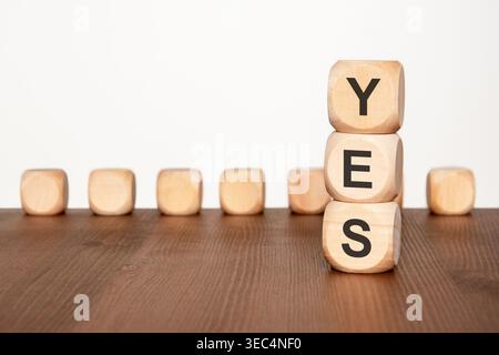Una pila di blocchi di legno che SI scrive SÌ si distingue contro una fila di blocchi vuoti sfocati su un tavolo di legno. Un solido concetto di business per l'accordo, appro Foto Stock