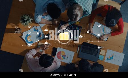 Un gruppo eterogeneo di professionisti collabora in uno spazio di lavoro moderno, analizzando le visualizzazioni dei dati e discutendo le strategie aziendali utilizzando il digitale Foto Stock
