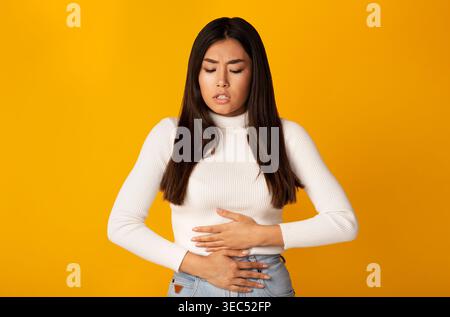 Sensazione di disagio mentre si tiene lo stomaco davanti allo sfondo giallo brillante a mezzogiorno Foto Stock