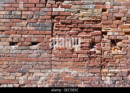 Pareti in mattoni con varie tonalità arancioni, linee di cemento, fori e mattoni decaduti, che mostrano una vecchia apertura in mattoni in vista orizzontale. Foto Stock