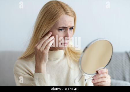 Matura donna triste guardando le rughe in specchio Foto Stock