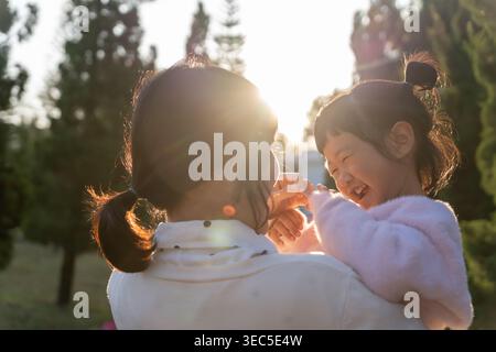 Mamma che abbraccia e porta la figlia che gioca insieme all'aperto sviluppo e crescita dell'infanzia della famiglia con amore per la preoccupazione della mamma sogno del bambino felice su Foto Stock