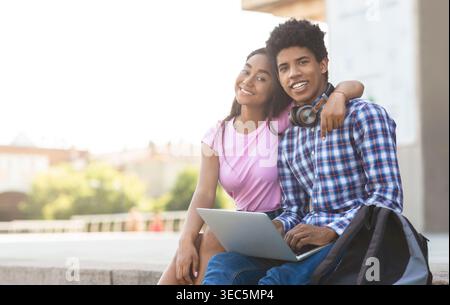 Giovani amici che si godono una giornata di sole mentre studiano insieme all'aperto vicino a un paesaggio cittadino Foto Stock