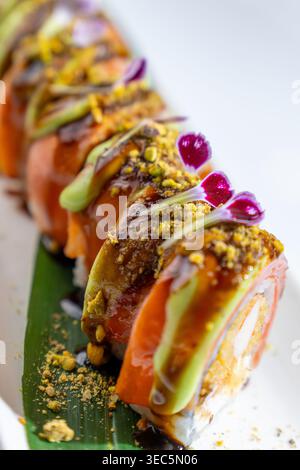 Sushi roll gourmet con tempura di gamberi, salmone e avocado. Condito con salsa e fiore commestibile. Primo piano della cucina giapponese. Foto Stock