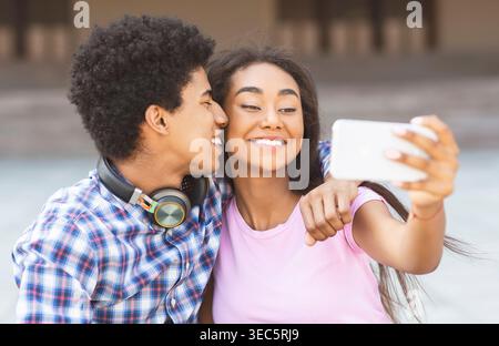 Una giovane coppia gode di un momento di gioia mentre si fa un selfie all'aperto al tramonto Foto Stock