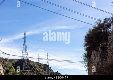 Torri di trasmissione dell'energia elettrica che trasportano cavi ad alta tensione su colline sotto un cielo blu, rappresentando infrastrutture ed energia Foto Stock