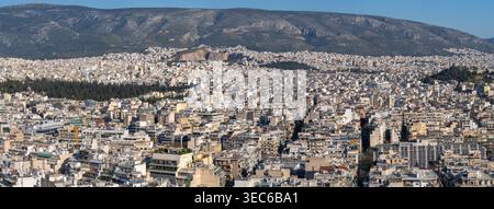 Una vista panoramica grandangolare del denso tessuto urbano di Atene, che si estende verso il maestoso Monte Imettus sotto un cielo limpido. Foto Stock