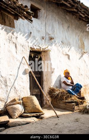 Un uomo che indossa un turbante giallo si siede a proprio agio su una pila di fieno fuori da una tradizionale casa dipinta di bianco a Bihar, in India, la scena raffigura un momento di Re Foto Stock