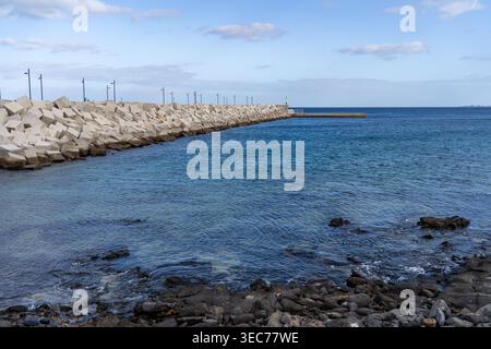 Una splendida scena costiera a Lanzarote caratterizzata da una frangiflutti in cemento e splendide acque turchesi in una giornata di sole. Foto Stock