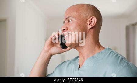 Professionista medico maschile in Scrubs parlare al telefono durante la consultazione telesanitaria domestica Foto Stock