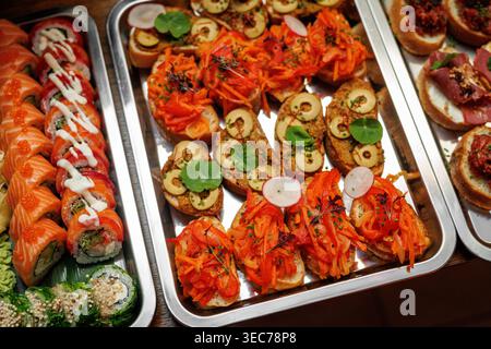 Una varietà di antipasti, tra cui involtini di salmone freschi e pane tostato con pepe rosso e guarnizioni di olive esposte su vassoi di metallo. Foto Stock