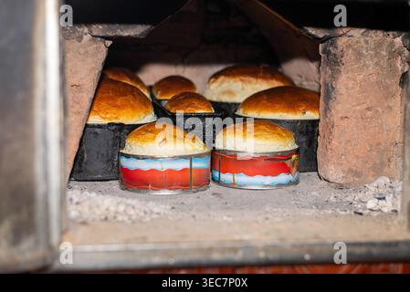 Cottura del pane fatta in casa in un forno in piccoli contenitori di metallo, processo di cottura tradizionale con crosta dorata e atmosfera rustica da cucina. Foto Stock